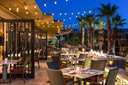 Outdoor dining area with string lights and palm trees to the right