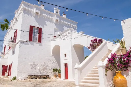 White stone building with red windows and doors, with a stairway on the right