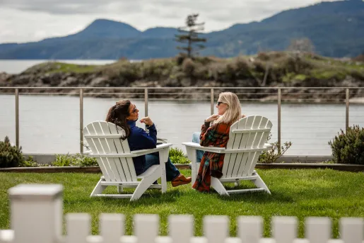 two guests in Adirondack chairs overlooking the water
