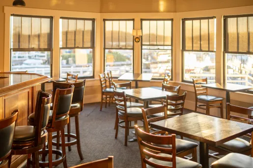 Indoor dining area surrounded by windows, looking out towards a harbor