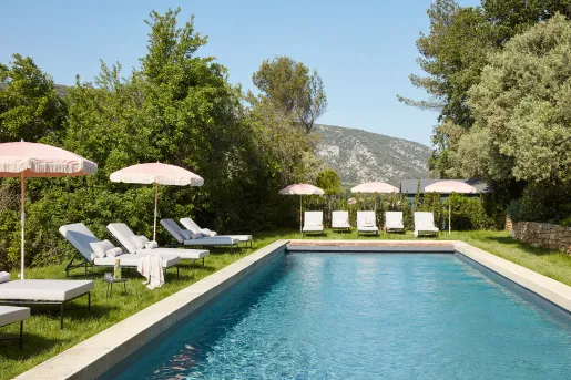 Outdoor pool surrounded by reclining chairs and umbrellas, with mountains in the distance