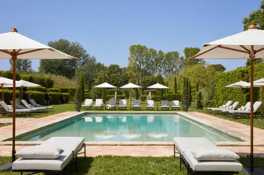 Outdoor pool with reclining pool chairs, surrounded by trees