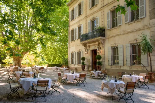 Outdoor dining area with circular tables next to a rustic, yellow building