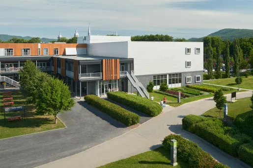 Exterior view of a gray stone building, with wooden accents and trimmed bushes in the front