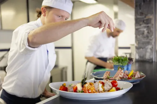 Chef preparing a plate of food, including kabobs and salads