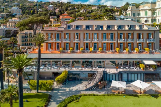 Exterior view of an orange and white hotel building with outdoor patios and palm trees in front
