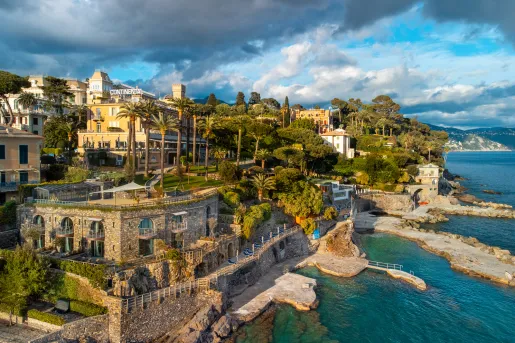 Exterior view of a stone building next to the ocean, with tall trees in the background