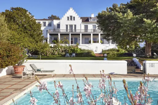 Exterior view of white and brown hotel building, with a large grass field and pool in front