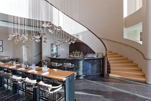 Bar and lounge with a large staircase to the right and hanging light fixtures
