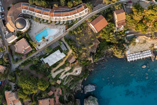 Sky view of white and tan buildings with an outdoor pool next to the shore of an ocean