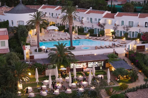 Sky view of white and tan buildings with an outdoor pool and tall palm trees