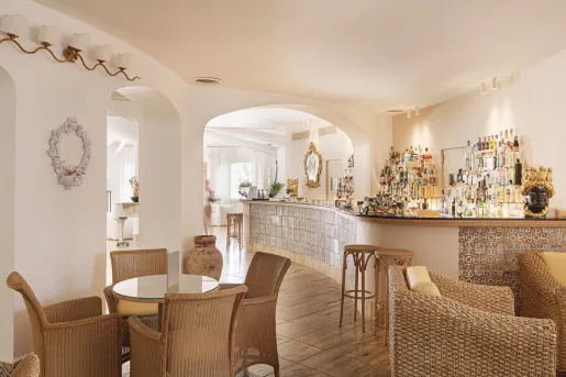 Bar and lounge with white walls, tiles on the bar, and woven chars around each table