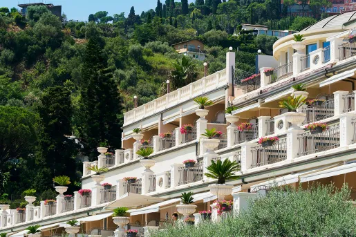 White hotel building with outdoor balconies, covered with pink and red flowers