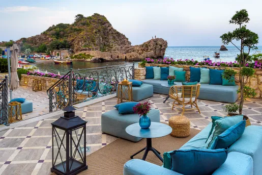 Outdoor patio with blue, cushioned chairs, looking out towards the ocean