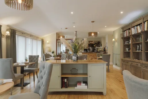Indoor dining tables with wine glasses and a wooden counter with a vase in the center