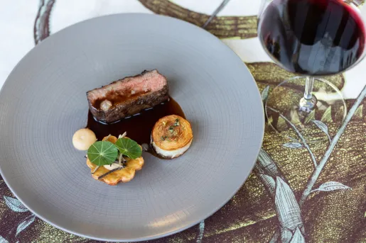 Gray plate with meat small pieces of meat and potatoes, next to a glass of wine