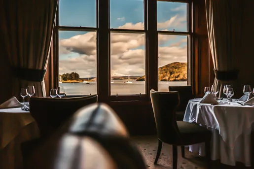 Dining tables with wine glasses and large windows looking out to a lake