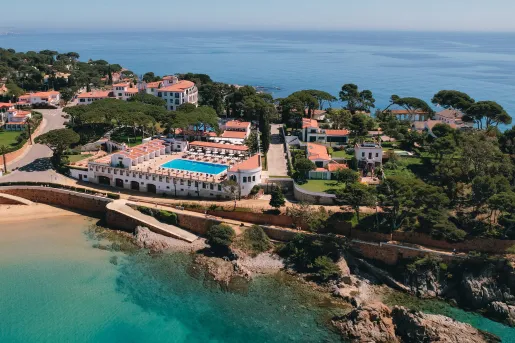 Sky view of buildings surrounded by tees on a cliff next to the ocean