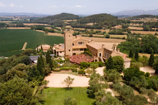 Sky view of rustic, stone building surrounded by trees and grass valleys