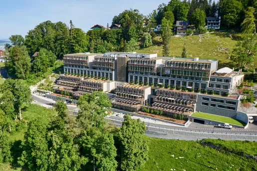 Exterior view of a long hotel complex, with large windows and tall trees