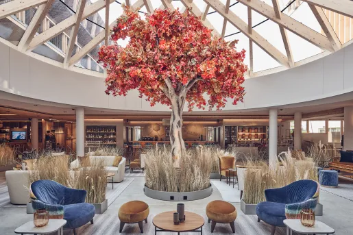 Large, indoor lobby with a glass ceiling and a large red tree in the middle