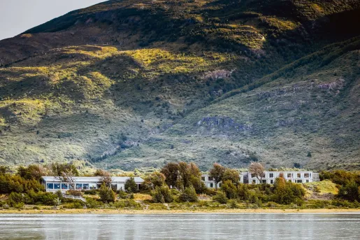 Long white hotel building surrounded by trees and a large hill