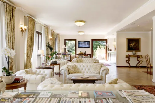 Indoor lobby with white, cushioned chairs and open doors leading to an outdoor garden