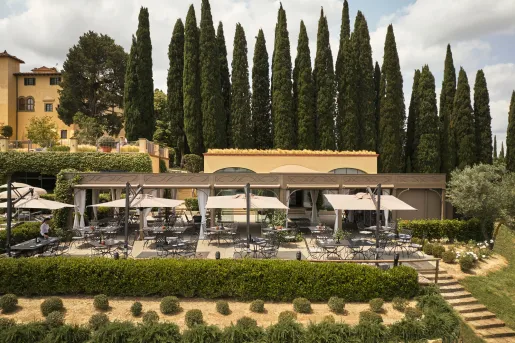 Outdoor garden and patio, with trimmed bushes and black chairs and tables