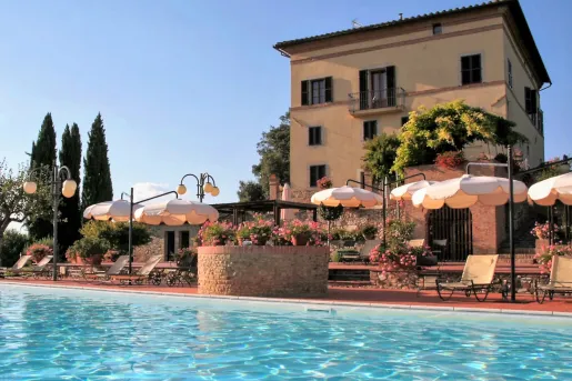 Outdoor pool in front of a hotel building, surrounded by umbrellas