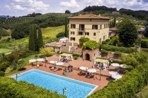 Hotel building with an outdoor pool and lounge, surrounded by trees and green plants