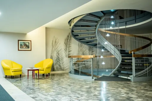 Room with a gray, spiral staircase with two yellow chairs on the left