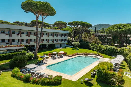 Outdoor pool surrounded by plants and bushes, next to a hotel building