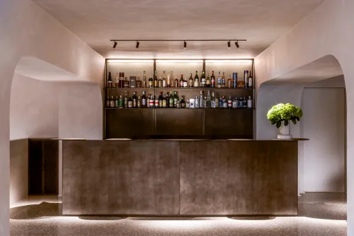 Gray bar counter with liquor on a shelf on the wall, illuminated by lights