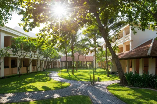 Outdoor courtyard between two white buildings, with a grass field and small palm trees
