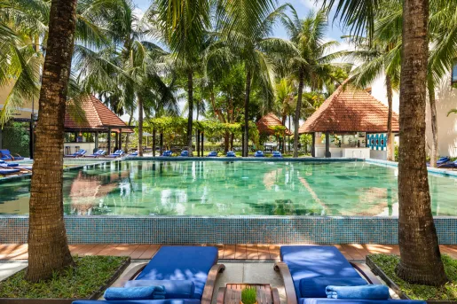 Outdoor pool with small huts and blue, reclining chairs surrounding the pool