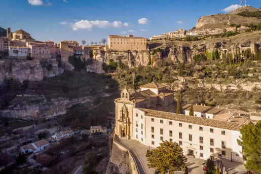 Rustic, cathedral-like buildings on a cliff, with smaller houses on the ground level
