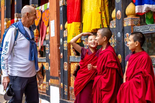 Man smiling and looking at 3 monk children in robes