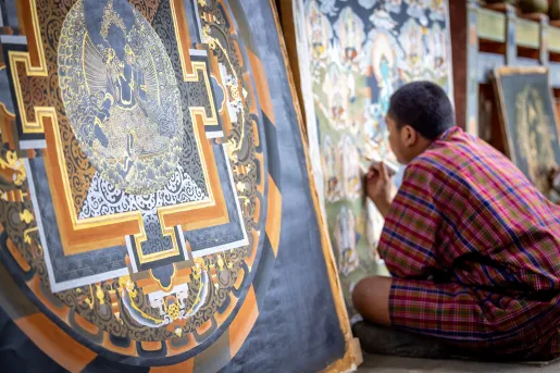 Man in monk attire painting a portrait while sitting on the ground