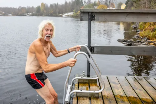 Older man hanging onto railing before jumping into a cold lake