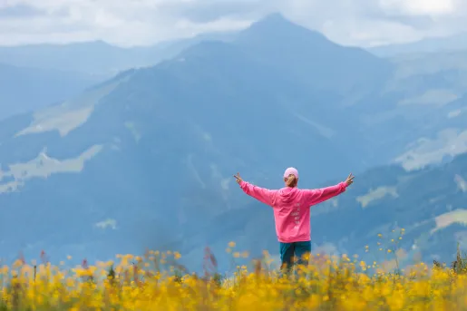 Woman wearing a pink jacket on top of a hill with her arms open