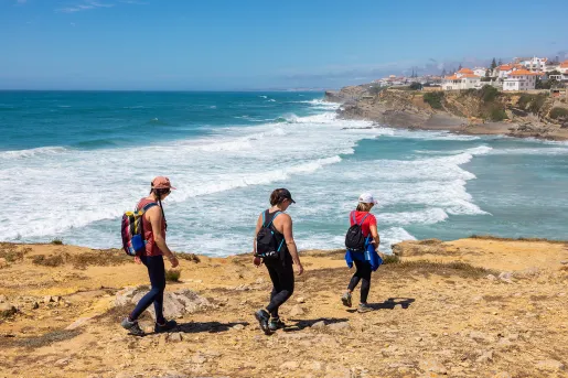 Three women descending down a dirt path towards a beach