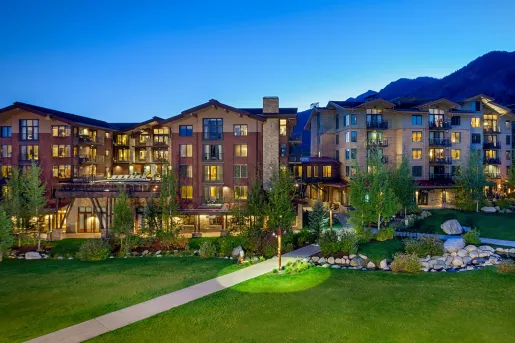 Wide, exterior view of stone hotel buildings with a large grass field in front
