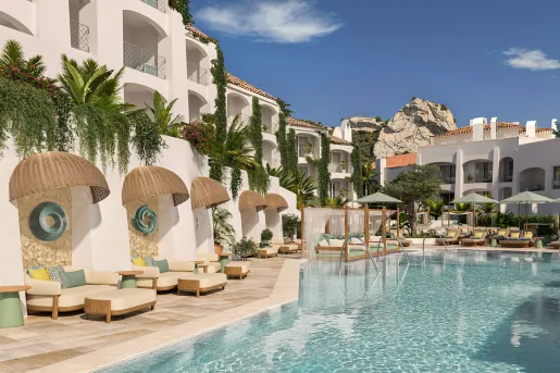 Outdoor pool with a white hotel building in the background and cushioned sofas surrounding the pool