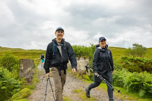 Man and woman holding hiking poles, walking on a dirt trial