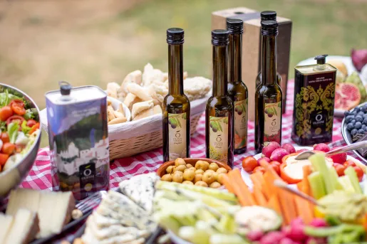 Table full of vegetables and snacks, and 5 bottles of olive oil