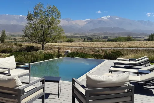 Outdoor pool surrounded by white, cushioned chairs in a valley with mountains in the background