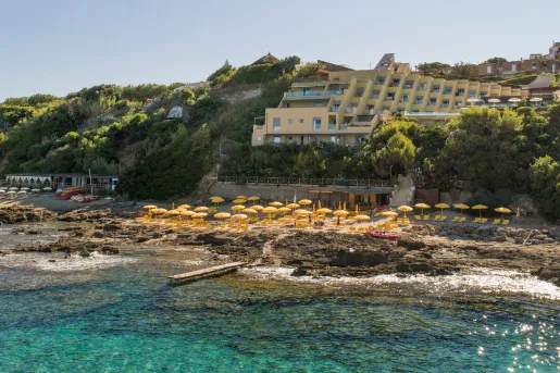 Ocean with a cluster of yellow umbrellas and chairs on a rock path, with a building in the background