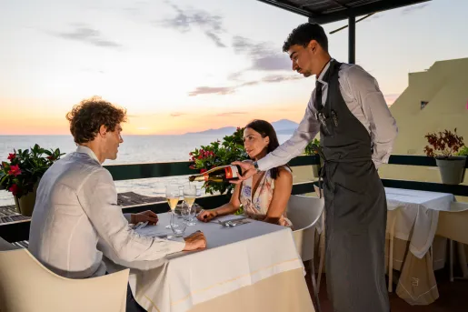 Man and woman dining at a table, with a waiter pouring wine into two glasses