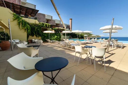 Outdoor patio with beige chairs in front of black tables, with a stone building in the background