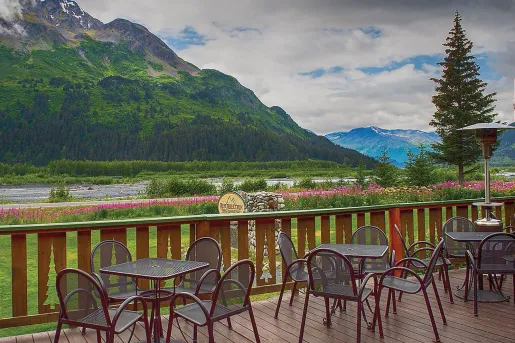Outdoor balcony and patio with metal chairs and tables, looking out towards a large mountain